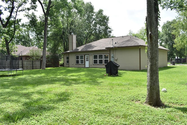 back of property featuring a lawn, a trampoline, fence, and a chimney