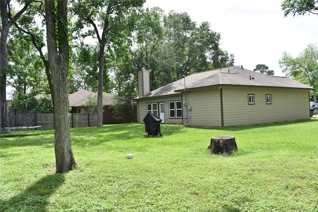 rear view of house with a fire pit, fence, a chimney, a trampoline, and a yard