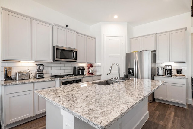 13716 Rising Sun Ln, Conroe, TX 77384 - kitchen featuring stainless steel appliances, backsplash, dark wood-style floors, light stone counters, and an island with sink