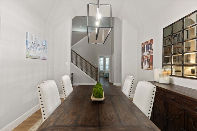 dining space featuring stairway, baseboards, high vaulted ceiling, and wood finished floors