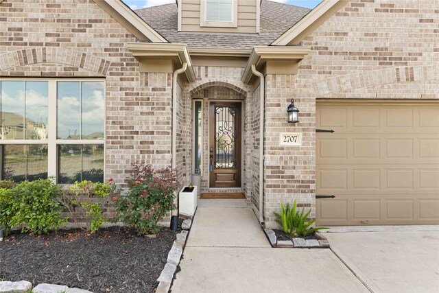 entrance to property with roof with shingles, concrete driveway, brick siding, and a garage