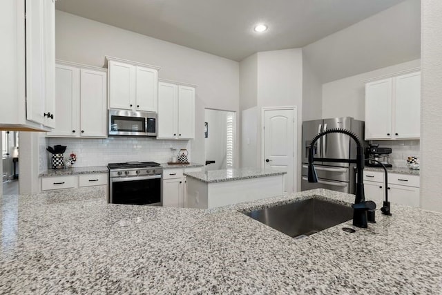 kitchen featuring white cabinets, appliances with stainless steel finishes, light stone counters, a sink, and decorative backsplash