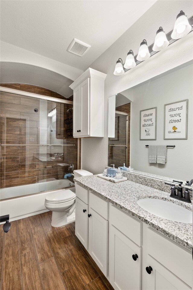 full bathroom featuring visible vents, vanity, wood finished floors, toilet, and combined bath / shower with glass door