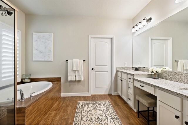 bathroom featuring double vanity, baseboards, wood finished floors, and a bath