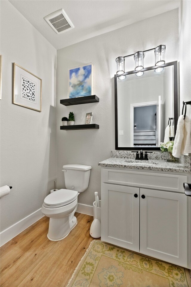 half bathroom featuring visible vents, wood finished floors, baseboards, vanity, and toilet