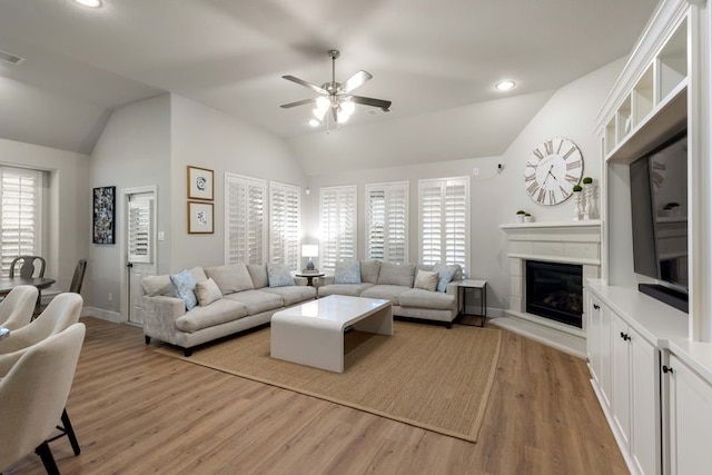 living room with light wood-style floors, a ceiling fan, a glass covered fireplace, and lofted ceiling