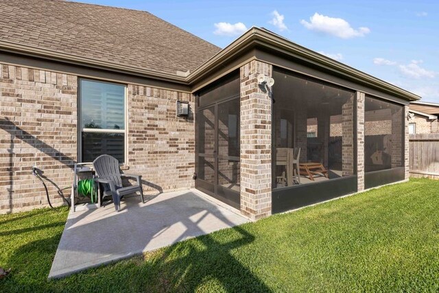 exterior space with brick siding, a shingled roof, a sunroom, a patio area, and a yard
