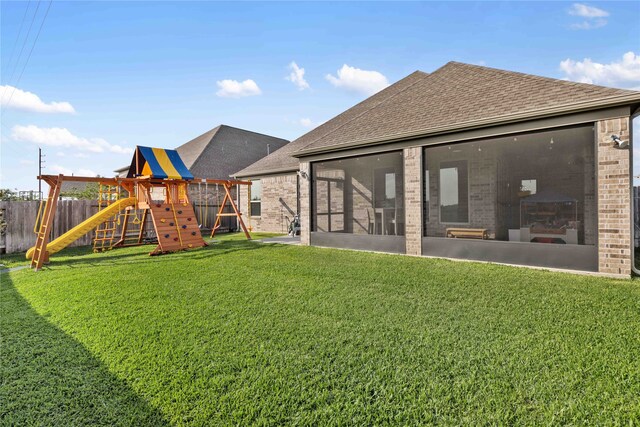 back of property featuring roof with shingles, a sunroom, brick siding, fence, and a playground
