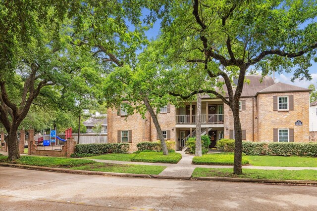 view of front of home with a playground, a balcony, a front lawn, and brick siding