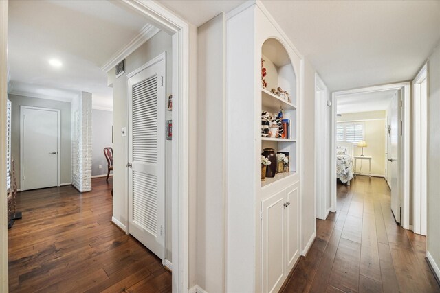 corridor featuring crown molding, built in features, dark wood-type flooring, and visible vents