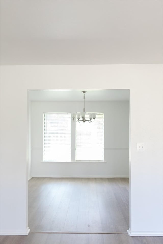 interior space with baseboards, a notable chandelier, plenty of natural light, and wood finished floors