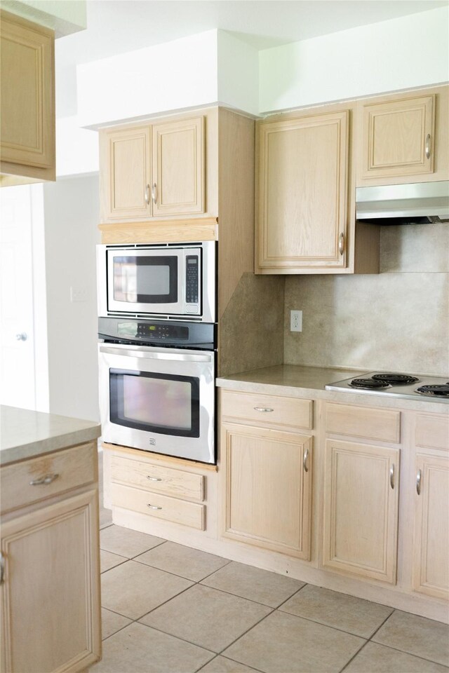 kitchen with light tile patterned floors, light brown cabinetry, appliances with stainless steel finishes, and under cabinet range hood