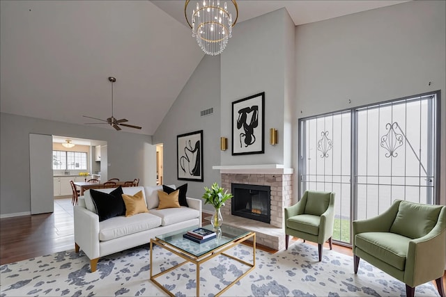 living area featuring visible vents, a glass covered fireplace, wood finished floors, baseboards, and high vaulted ceiling
