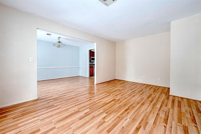 empty room with visible vents, light wood-style floors, and a notable chandelier