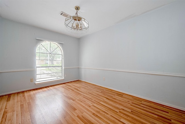 spare room with an inviting chandelier, light wood-style floors, baseboards, and visible vents