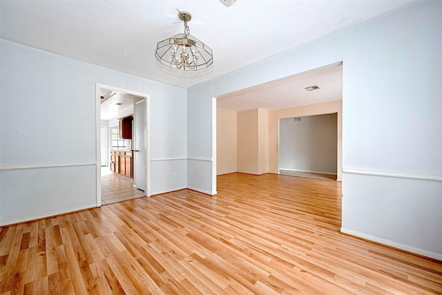 empty room featuring baseboards, light wood-style flooring, a chandelier, and visible vents