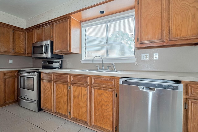 kitchen featuring brown cabinetry, a sink, light countertops, stainless steel appliances, and light tile patterned flooring