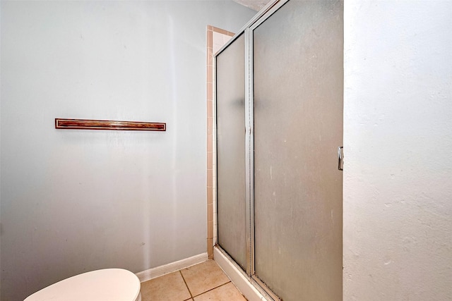 bathroom featuring tile patterned flooring, baseboards, toilet, and a shower stall