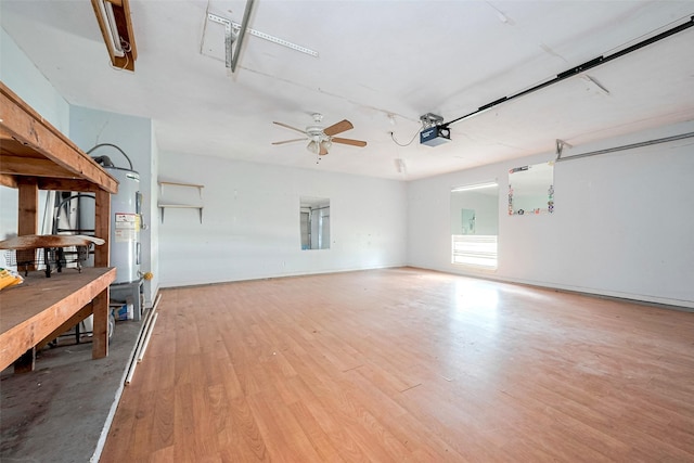 unfurnished living room with a garage, ceiling fan, light wood-style flooring, and electric water heater