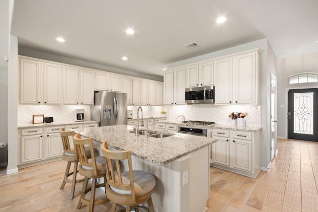 kitchen with a kitchen island with sink, recessed lighting, a sink, appliances with stainless steel finishes, and backsplash