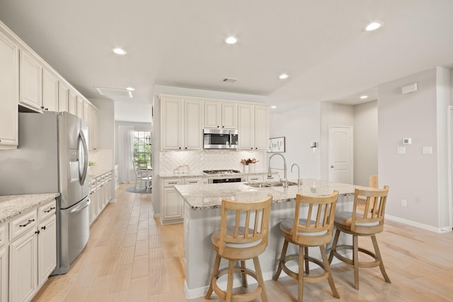 kitchen featuring backsplash, appliances with stainless steel finishes, a sink, and light wood-style floors