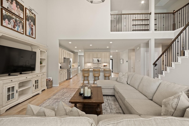 living area featuring light wood-type flooring, recessed lighting, stairs, and a towering ceiling