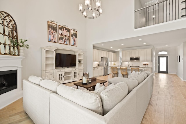 living room featuring baseboards, a fireplace with raised hearth, light wood finished floors, an inviting chandelier, and recessed lighting