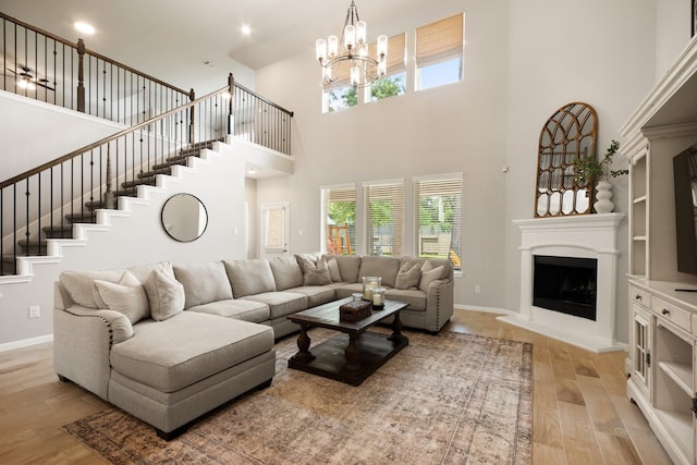 living room with baseboards, a high ceiling, a fireplace with raised hearth, a chandelier, and light wood-style flooring