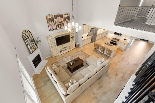 living room with a fireplace, baseboards, a notable chandelier, a high ceiling, and light wood-style flooring