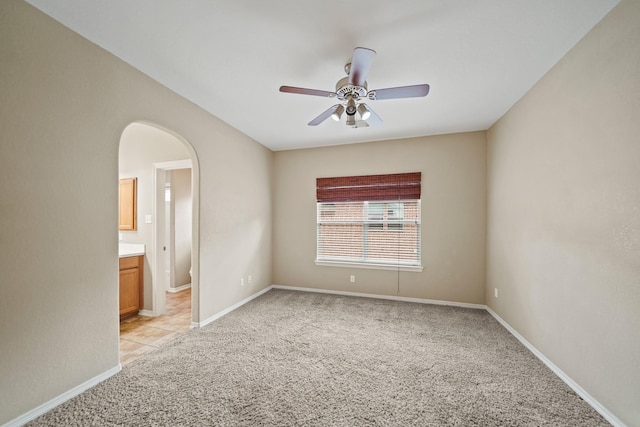 unfurnished room featuring light colored carpet, a ceiling fan, baseboards, and arched walkways
