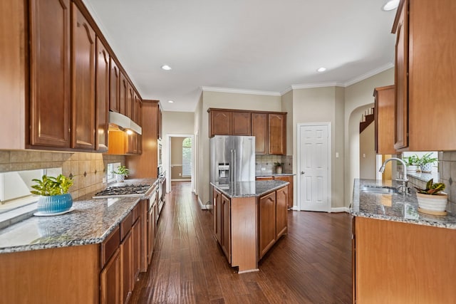 kitchen with backsplash, arched walkways, dark stone countertops, under cabinet range hood, and stainless steel appliances