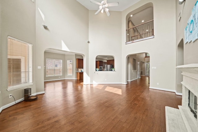 unfurnished living room featuring arched walkways, ceiling fan, a glass covered fireplace, and wood finished floors