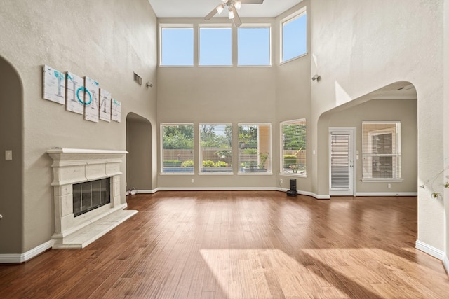 unfurnished living room featuring a healthy amount of sunlight, a ceiling fan, arched walkways, a glass covered fireplace, and a high ceiling