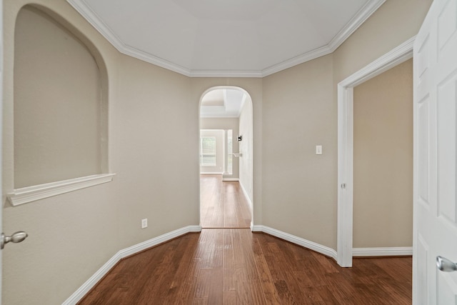 corridor featuring arched walkways, baseboards, ornamental molding, and wood finished floors