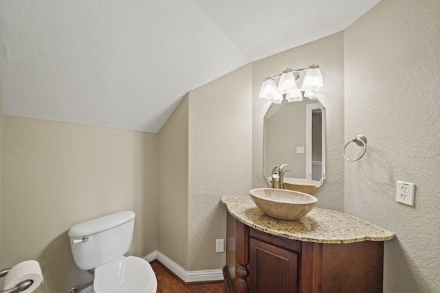 half bath with vanity, wood finished floors, toilet, baseboards, and vaulted ceiling