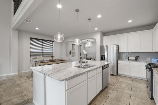 kitchen featuring a sink, appliances with stainless steel finishes, light tile patterned floors, and a center island with sink