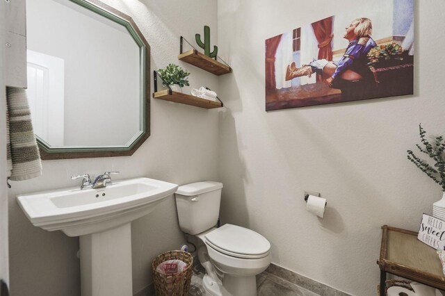 half bathroom with a sink, tile patterned flooring, and toilet