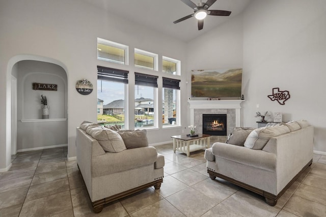 tiled living area featuring ceiling fan, baseboards, high vaulted ceiling, and a tile fireplace