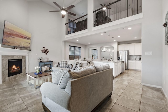 living room with a towering ceiling, light tile patterned flooring, a fireplace, baseboards, and ceiling fan