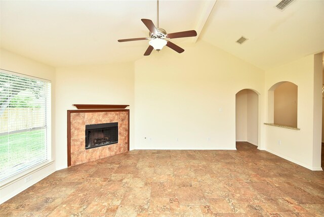 unfurnished living room with ceiling fan, lofted ceiling with beams, a tiled fireplace, stone finish flooring, and visible vents
