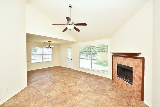 unfurnished living room featuring high vaulted ceiling, stone finish floor, ceiling fan with notable chandelier, baseboards, and a tile fireplace