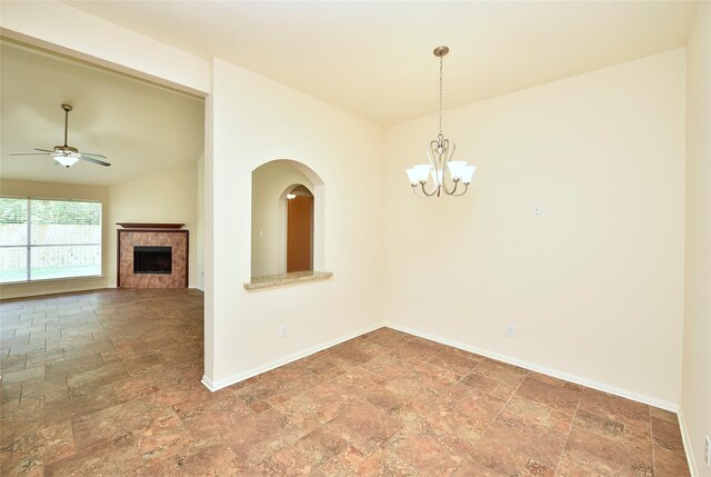 spare room featuring stone tile floors, baseboards, ceiling fan with notable chandelier, and a fireplace