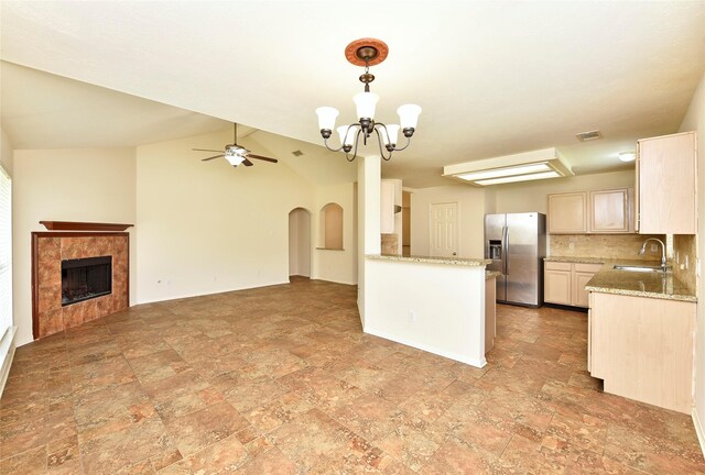 kitchen with stone finish floor, stainless steel refrigerator with ice dispenser, visible vents, a tile fireplace, and a sink