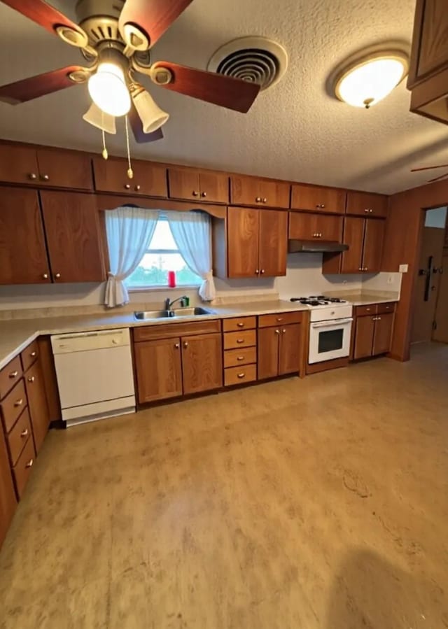 kitchen featuring ceiling fan, brown cabinets, a sink, under cabinet range hood, and white appliances