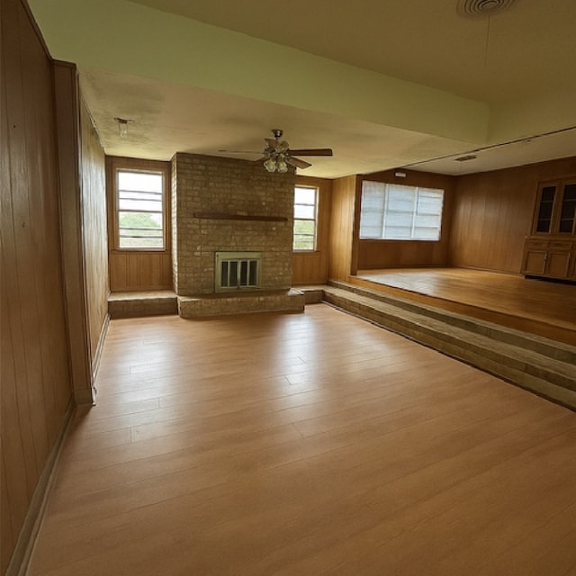 1904 Gun And Rod Rd, Brenham, TX 77833 - unfurnished living room with light wood-style flooring, wooden walls, healthy amount of natural light, ceiling fan, and a brick fireplace
