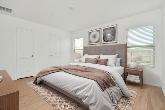 bedroom featuring baseboards, light wood-type flooring, and visible vents