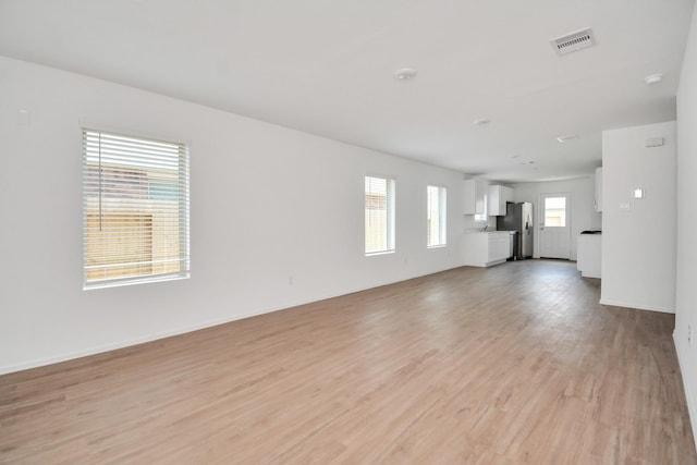 unfurnished living room featuring visible vents, baseboards, and light wood-type flooring