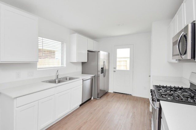 kitchen with light wood-style floors, a sink, white cabinetry, and appliances with stainless steel finishes