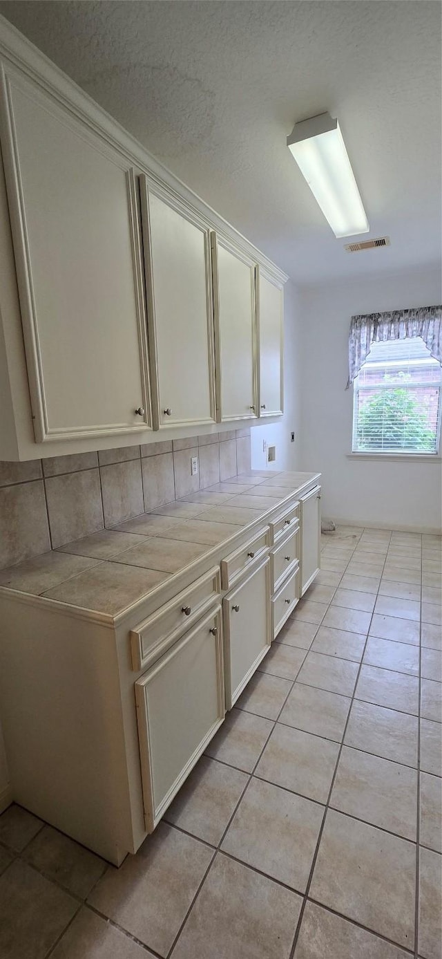 kitchen featuring backsplash, visible vents, light countertops, light tile patterned flooring, and white cabinetry