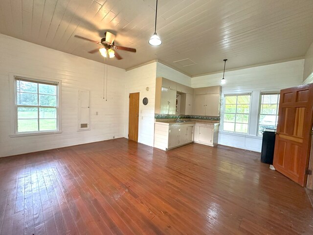 unfurnished living room featuring a healthy amount of sunlight, wooden ceiling, a ceiling fan, and dark wood-type flooring